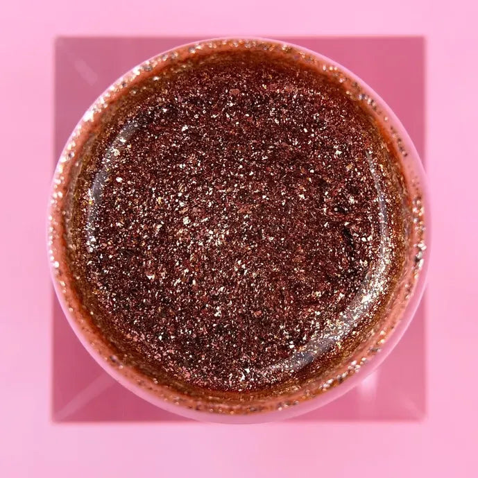 Open jar of rose gold glitter UV gel for manicure on a pink background