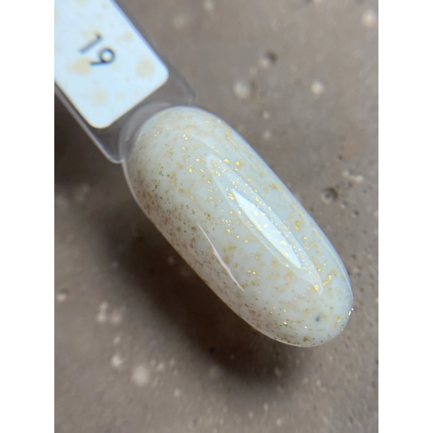 Swatch of white gel nail polish with fine gold glitter, shown on a nail tip