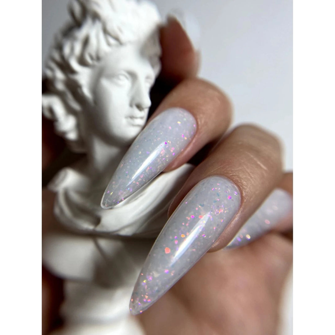 Hand with long almond-shaped nails in iridescent glitter gel polish holding a white statue