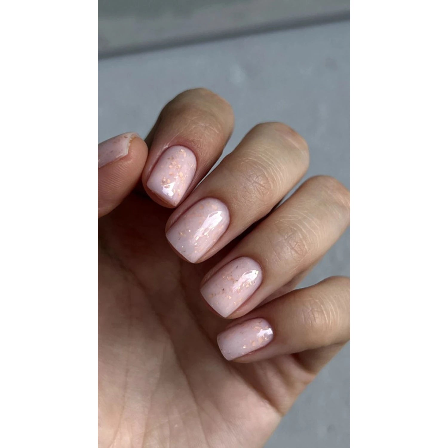 Short natural nails with glossy pale pink gel polish and subtle gold glitter flakes