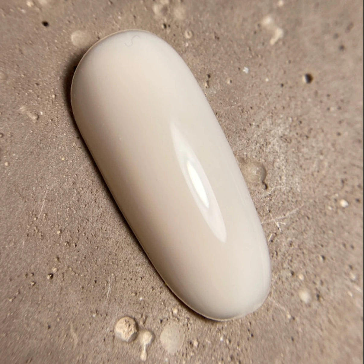 Neutral beige gel nail polish swatch on textured stone background, glossy finish