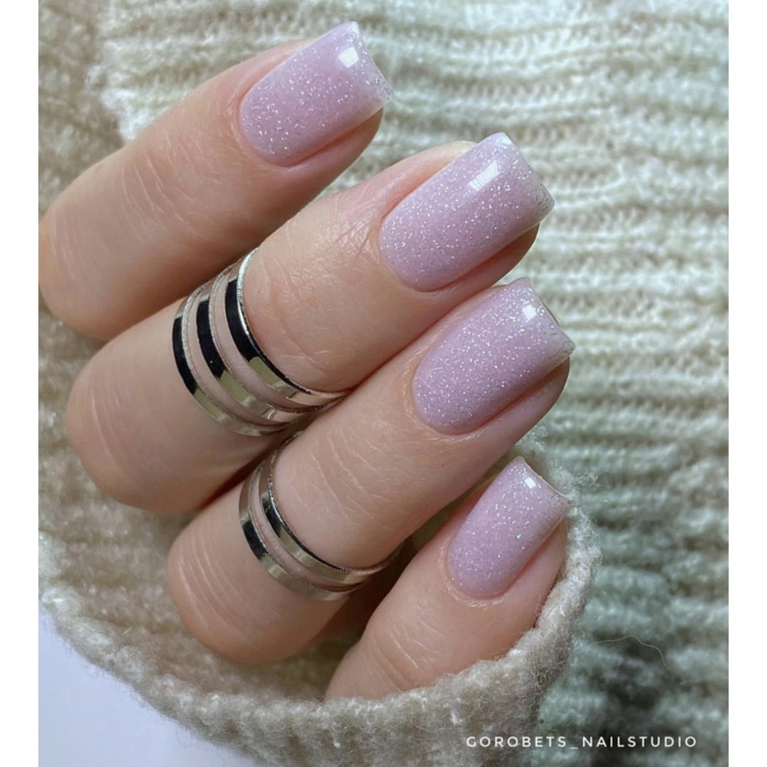 Hand with light pink glitter gel polish manicure, short square nails, silver rings