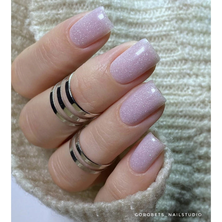 Hand with light pink glitter gel polish manicure, short square nails, silver rings