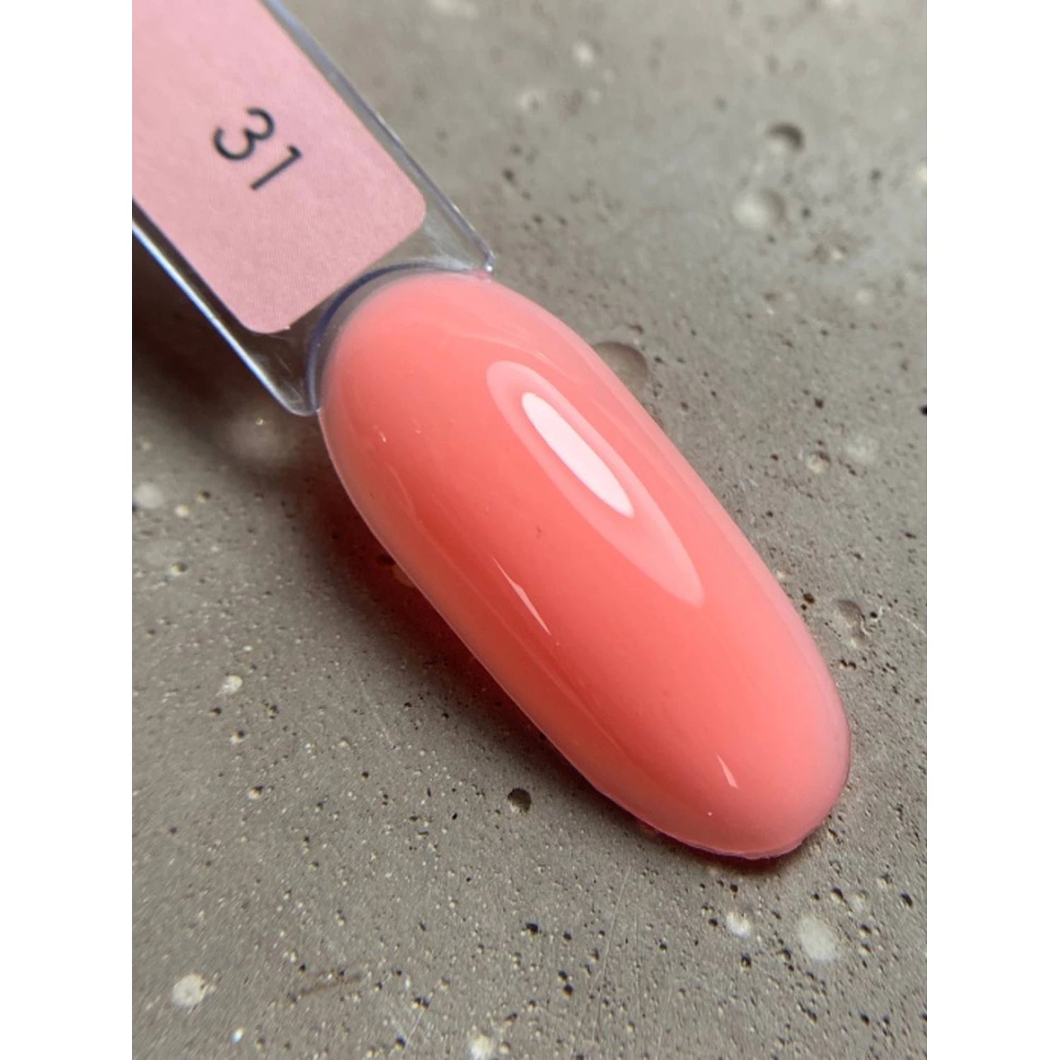 Swatch of glossy pink gel nail polish on a sample tip against a textured gray background