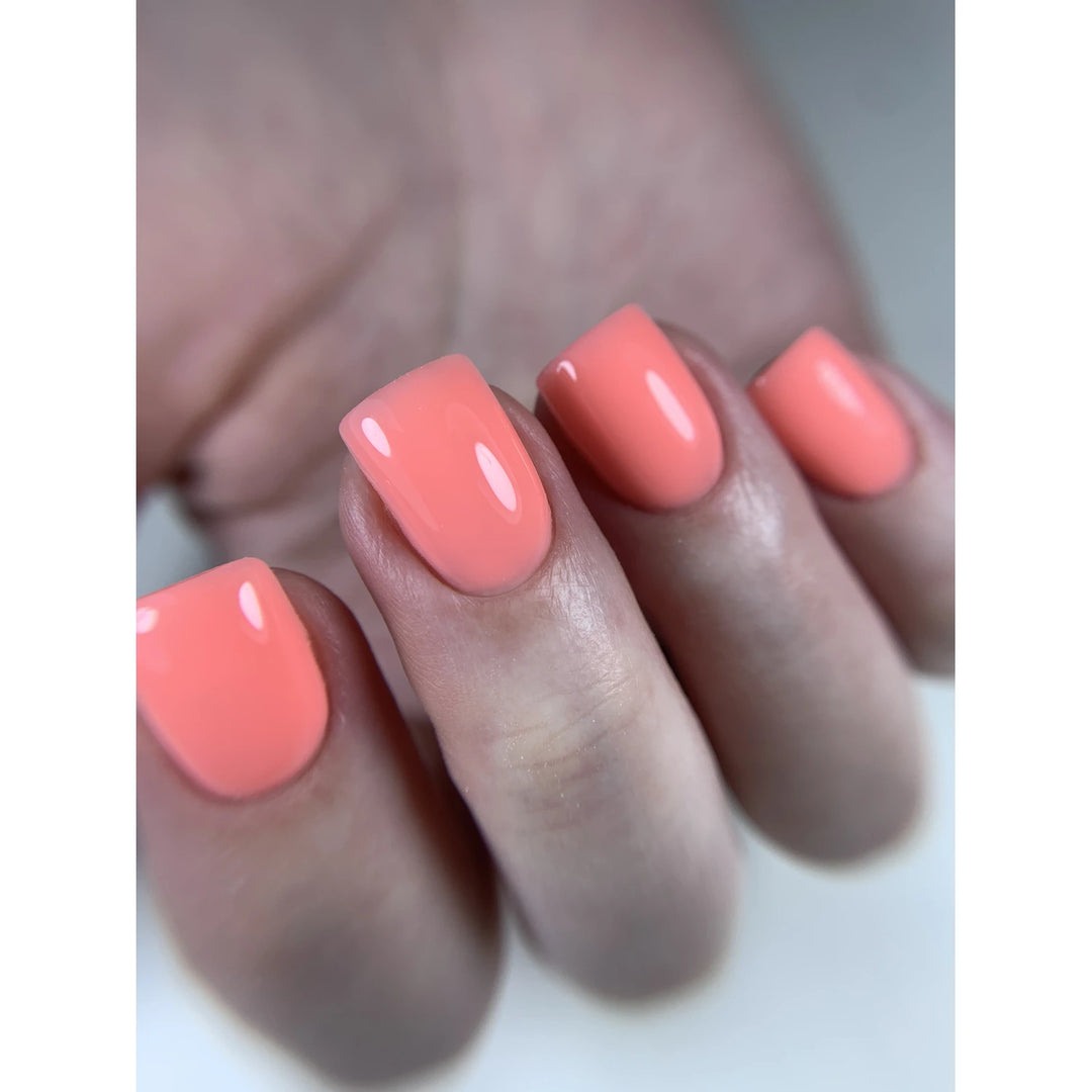 Close-up of manicured hand with glossy coral UV gel nail polish