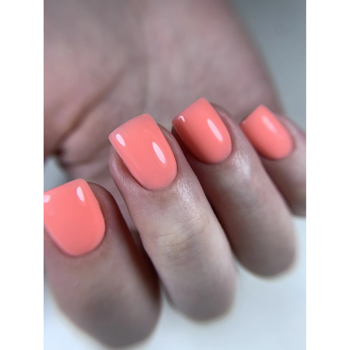 Close-up of manicured hand with glossy coral UV gel nail polish