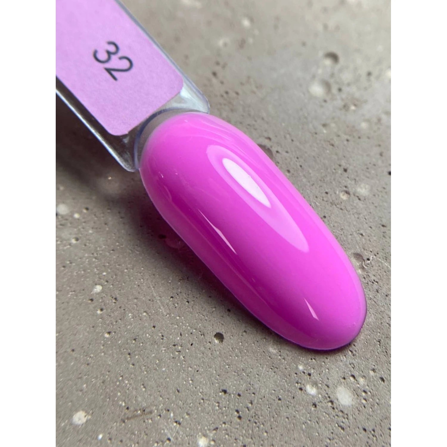 Swatch of glossy vibrant pink gel nail polish on a display stick against a stone background