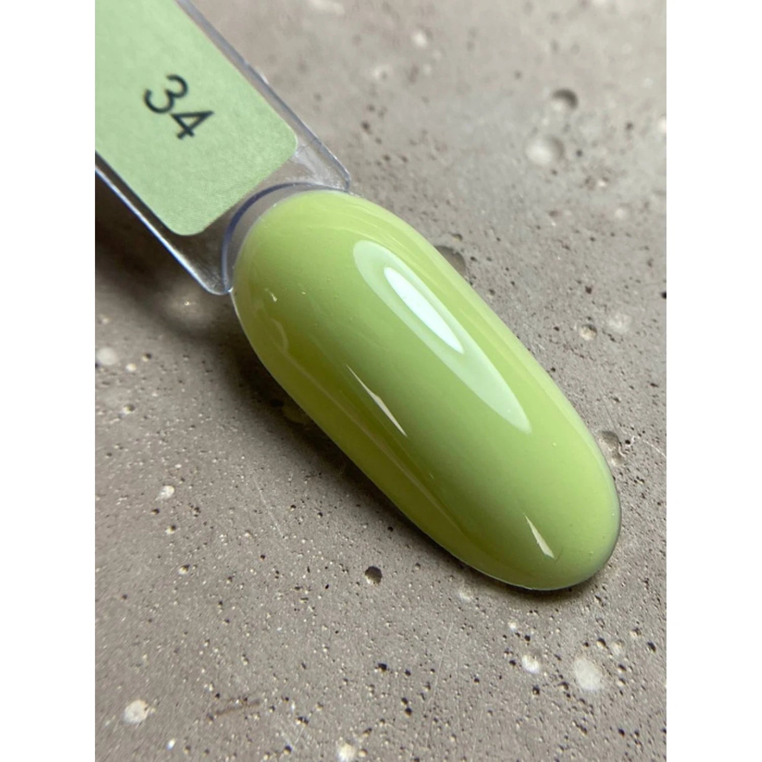 Lime green nail polish color sample on plastic swatch stick, shown on textured surface.