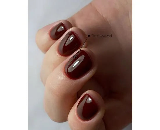 Hand with short nails painted in glossy dark red gel polish, labeled as Red wood shade.