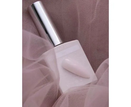 Light pink UV gel polish bottle with matching nail tip on soft pink tulle background