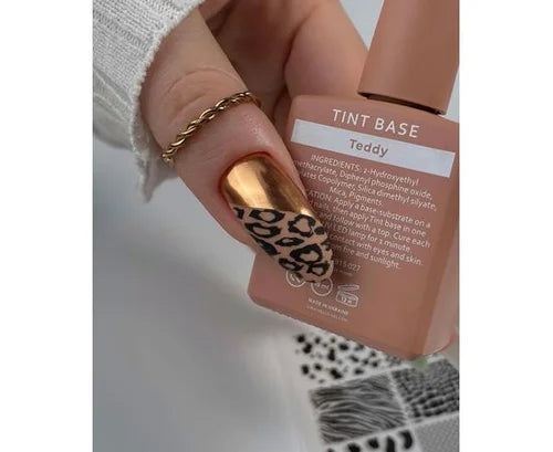 Hand with gold and leopard nail art holding Teddy tint base nail polish bottle.