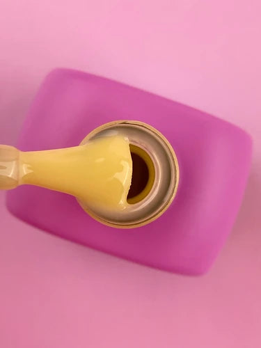 Open nail polish bottle with yellow gel polish and pink cap on pink background