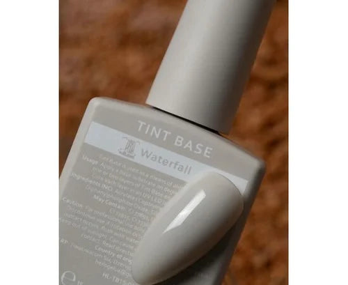 Bottle of Tint Base nail polish in Waterfall shade with matching swatch on brown background