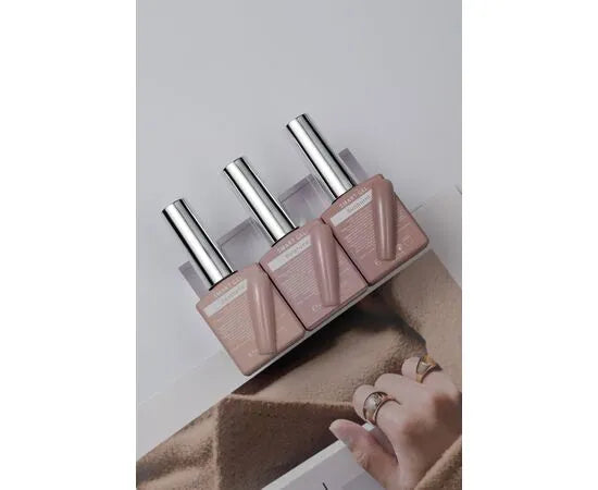 Three bottles of nude pink gel nail polish with silver caps, next to manicured hand with rings