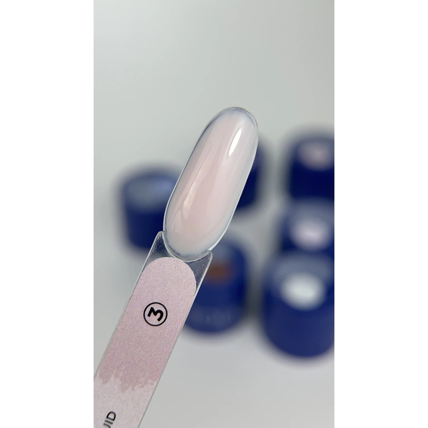 Milky pink UV gel nail polish swatch on nail tip with blue gel containers in background
