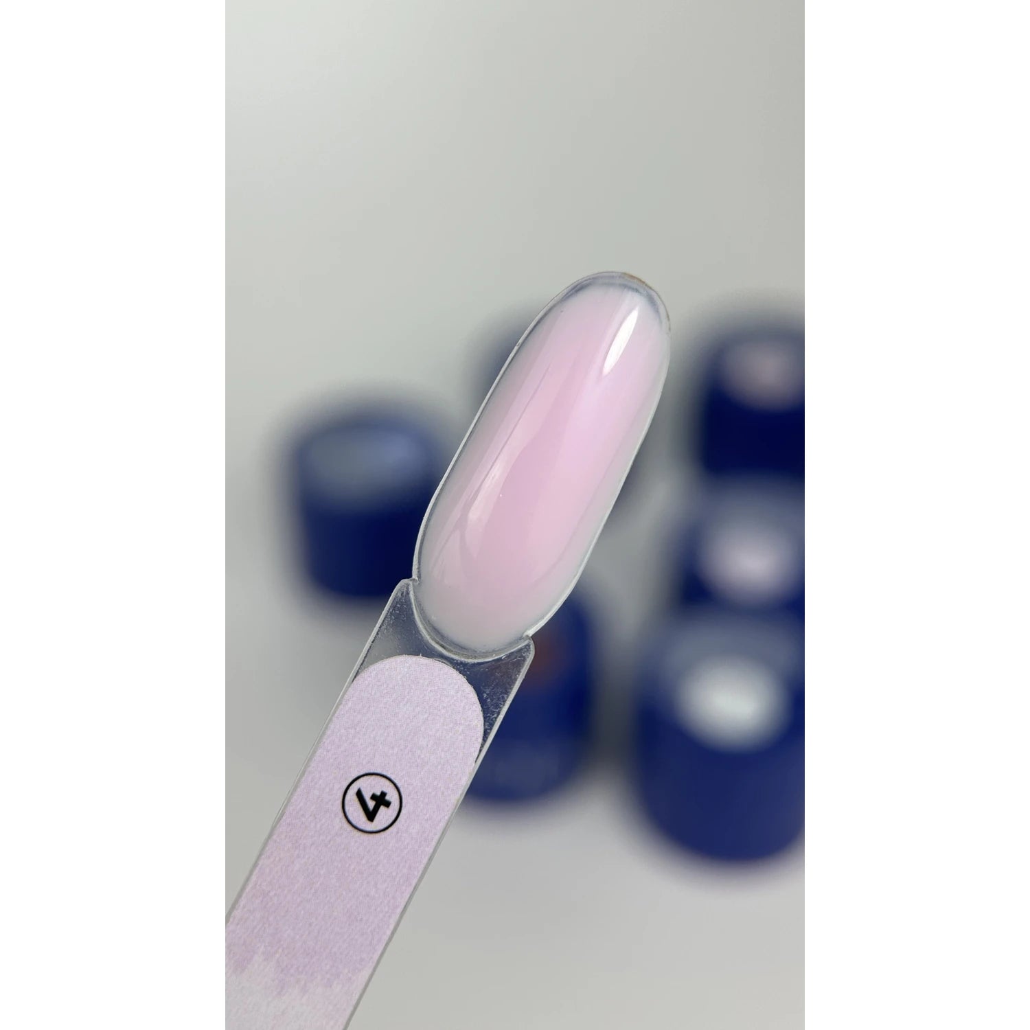 Swatch of light pink UV gel polish on nail display stick with blue containers in background