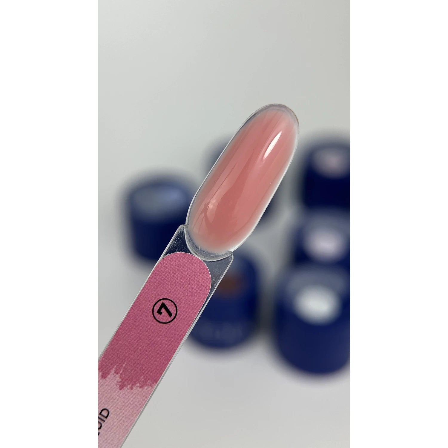 Swatch of glossy pink UV gel nail polish on nail display stick with blue jars blurred in background