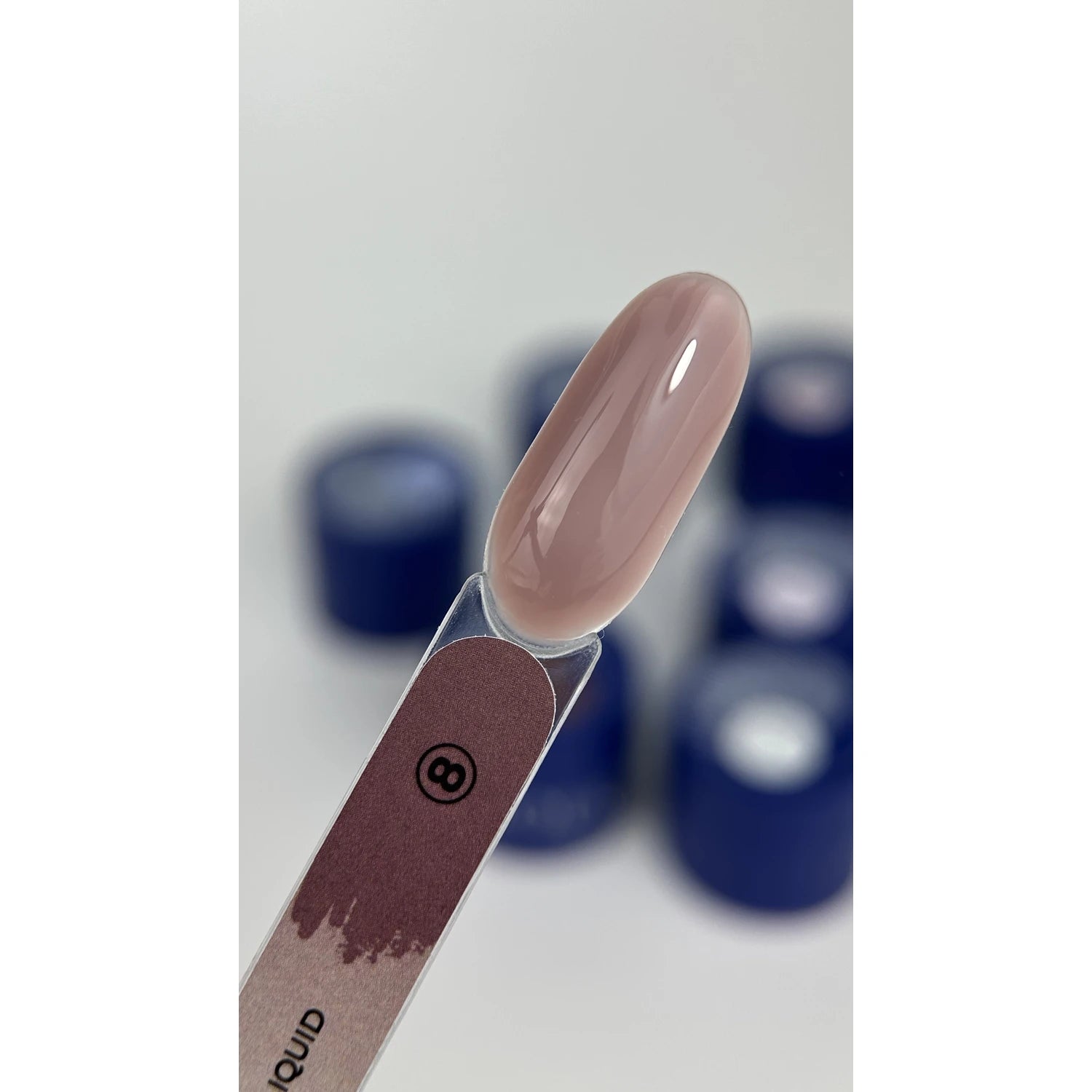 Nude pink gel nail polish swatch on sample tip with blue containers in background