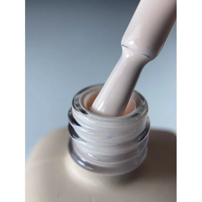 Close-up of a nail polish brush with light nude gel polish inside an open bottle