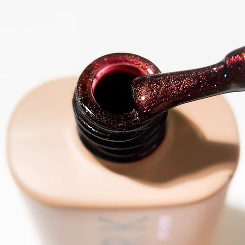 Shimmery red-brown gel nail polish on brush above open bottle, manicure product closeup