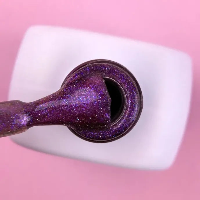 Purple cat eye gel nail polish with glitter, open bottle and applicator on pink background
