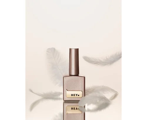 Shimmery nude nail polish bottle with gold label surrounded by soft white feathers.