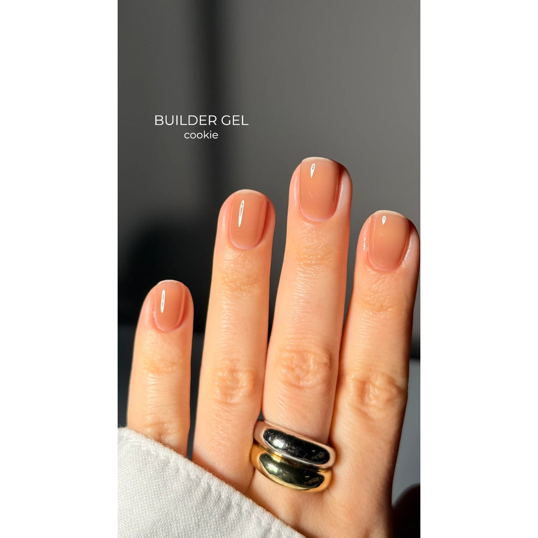 Hand with short, natural-shaped nails featuring nude builder gel polish in a cookie shade