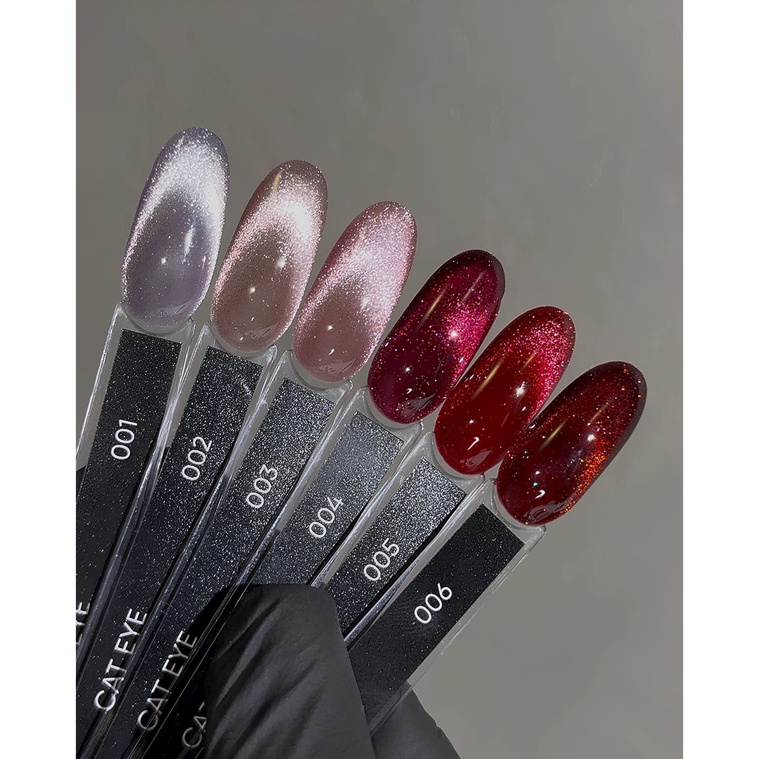 Cat eye gel nail polish swatches in glittery shades, numbered 001 to 006, on display sticks
