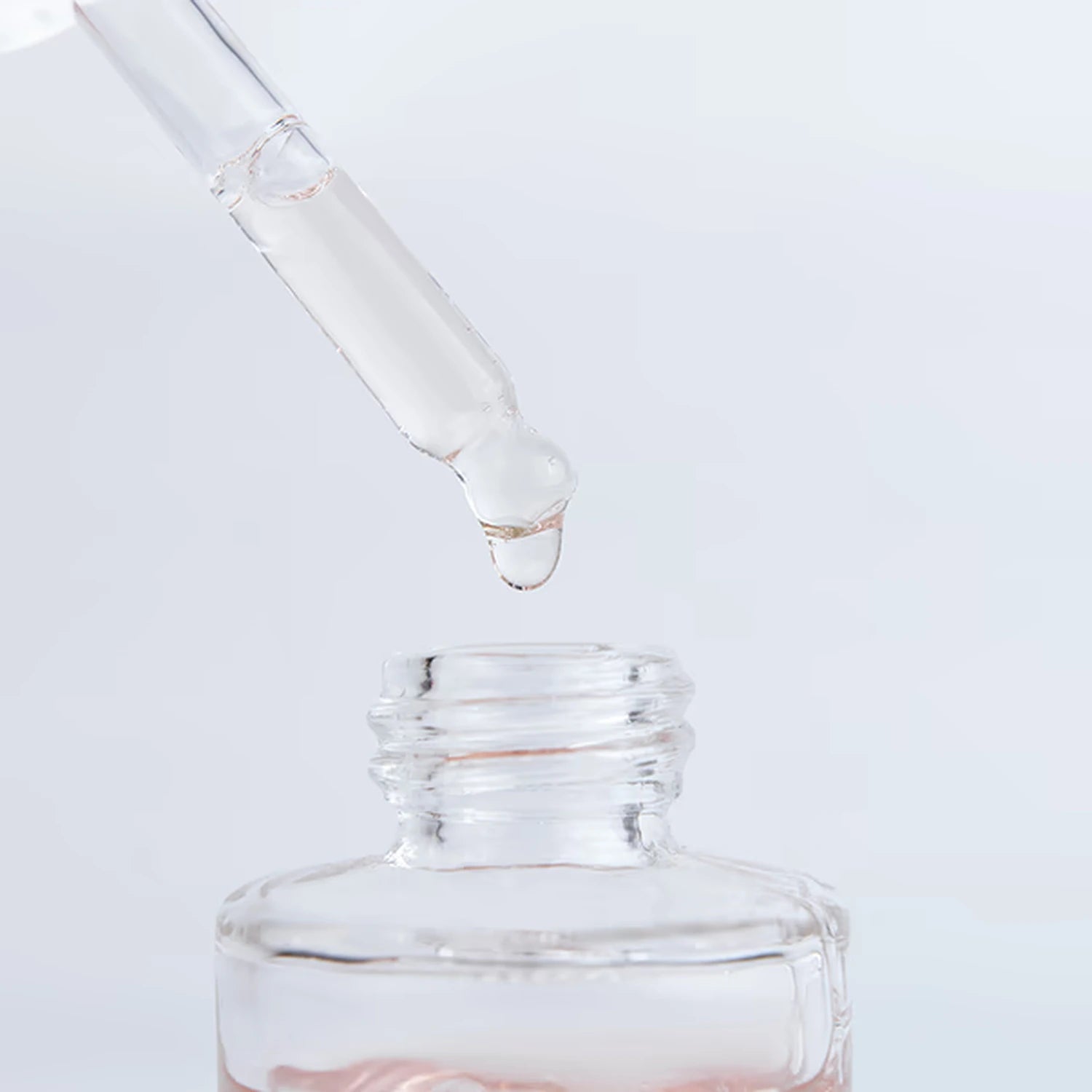Clear liquid dropper with serum above an open glass bottle, nail care remover product
