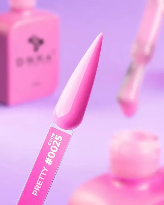 Pink gel nail polish sample on swatch stick, code 0025, with bottles in the background