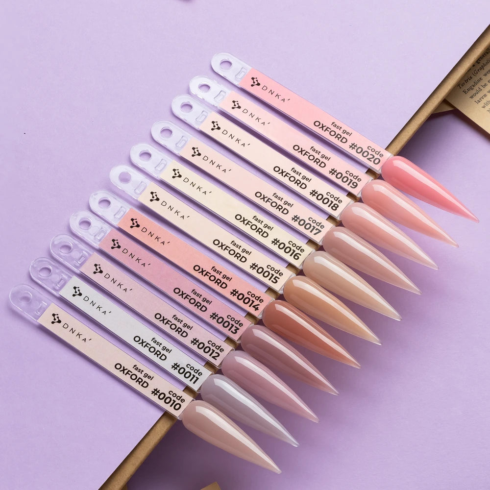 A set of ten Dinka Oxford nail polish sample sticks arranged diagonally on a lavender background, showing a gradient of nude pink, beige, and nude brown colors.