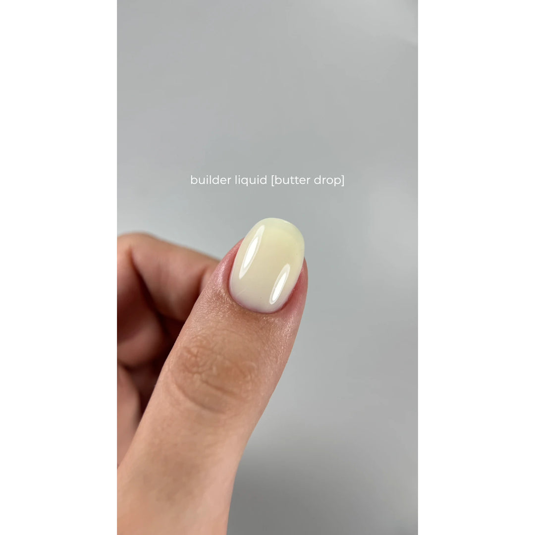 Thumb with glossy butter drop builder gel nail, showcasing soft yellow manicure finish.