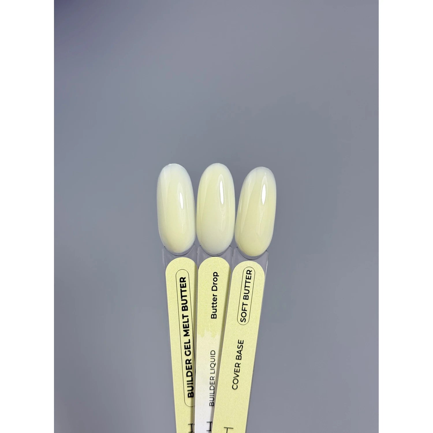 Three nail gel color swatches in pale yellow shades on labeled sticks for manicure