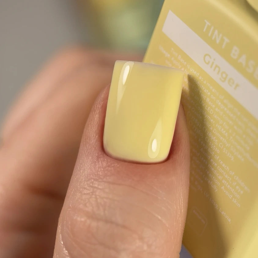 Close-up of a fingernail with glossy pale yellow gel polish, labeled Ginger tint base