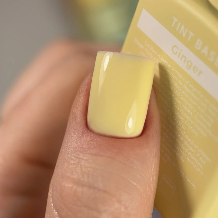 Close-up of a fingernail with glossy pale yellow gel polish, labeled Ginger tint base
