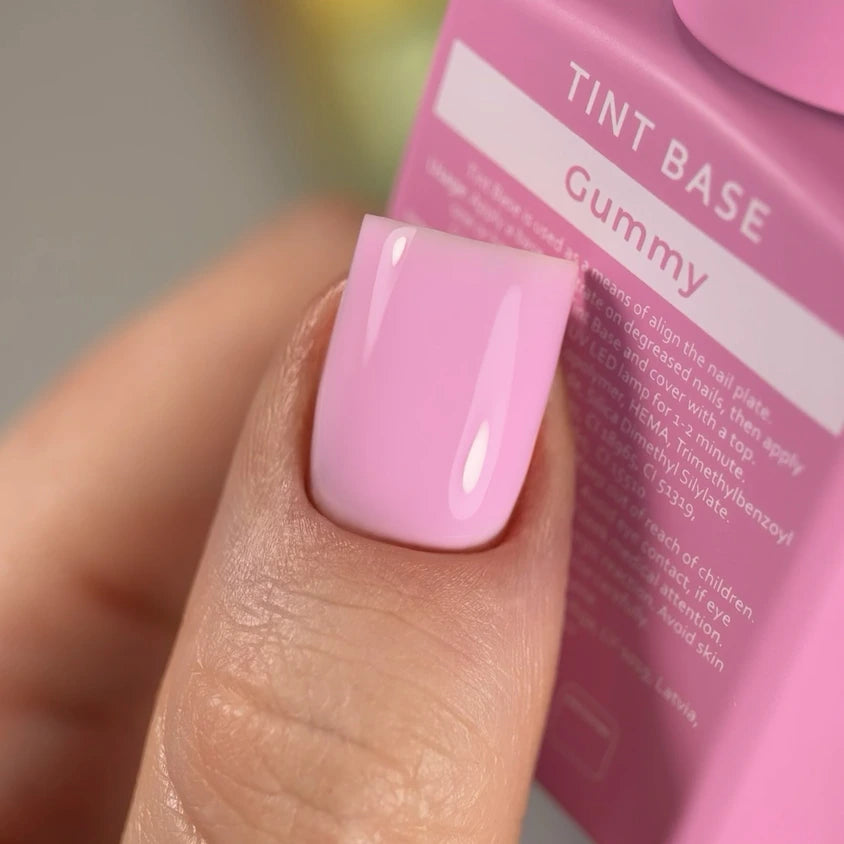 Close-up of a hand with glossy light pink gel polish manicure, holding pink nail tint base bottle.