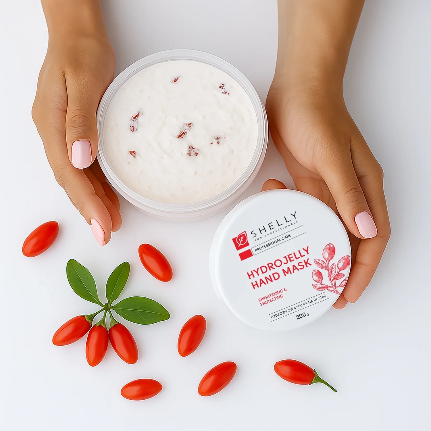 Hands holding hydrojelly hand mask jar, surrounded by red berries and green leaves, manicure visible.