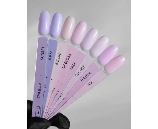Hand holding nail color swatches in pastel gel polish shades for manicure, labeled with names.