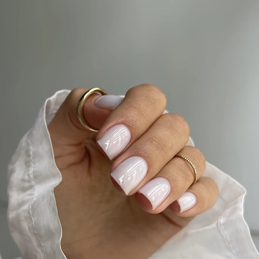 Hand with glossy pale pink gel manicure and gold rings, perfect nails close-up