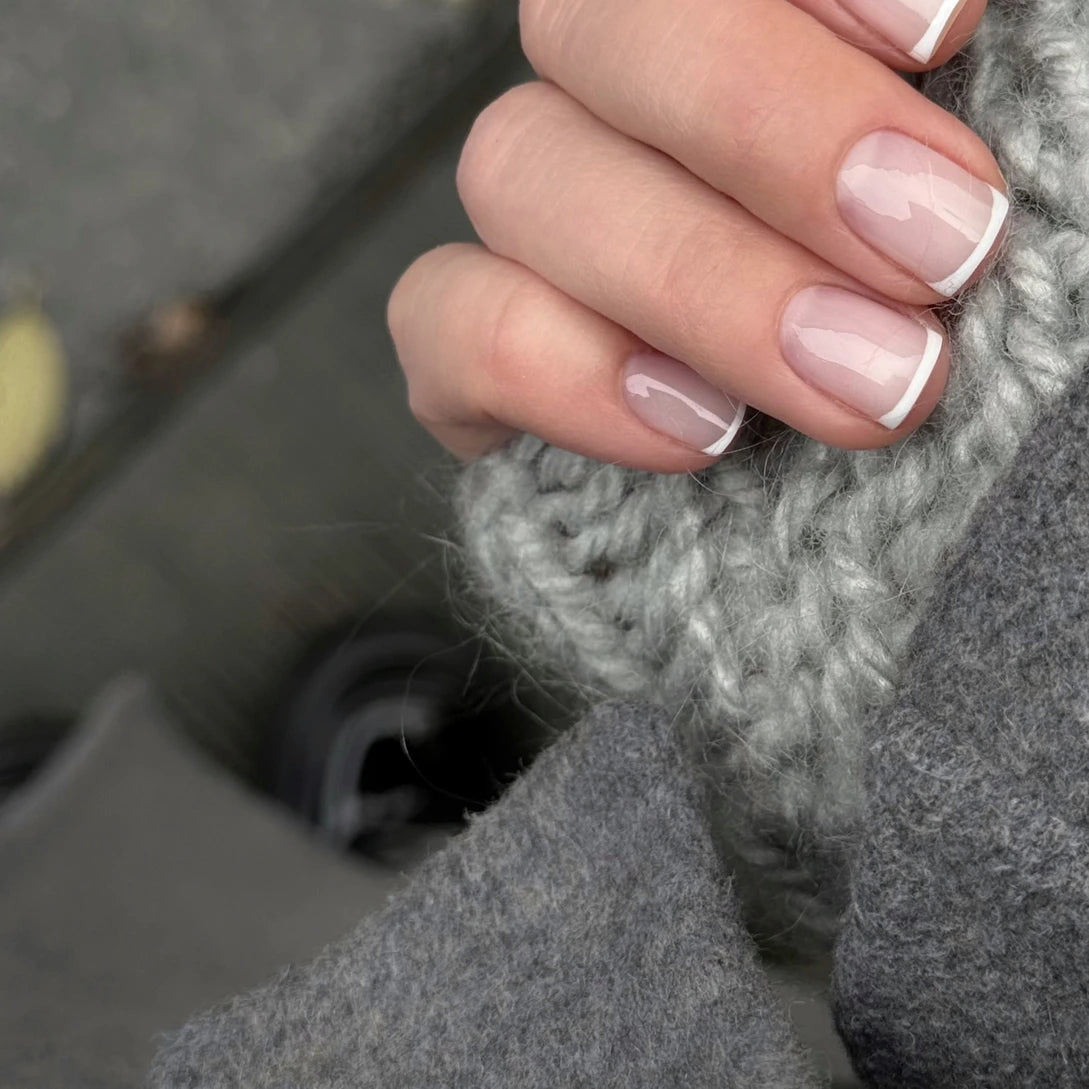 Hand with classic French manicure, short natural nails, holding gray knit fabric