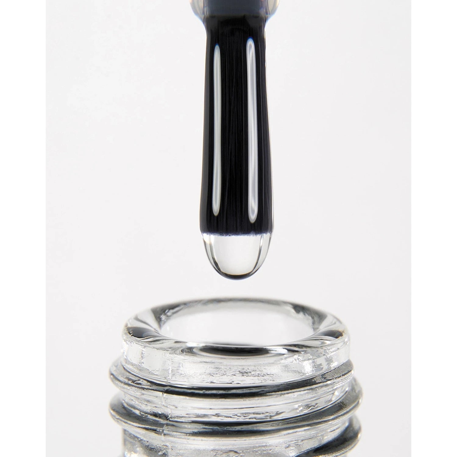 Close-up of a nail polish brush with clear gel above an open nail polish bottle