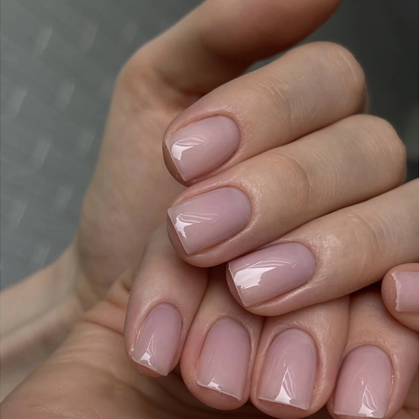 Short natural nails with glossy nude UV gel polish, professional manicure close-up