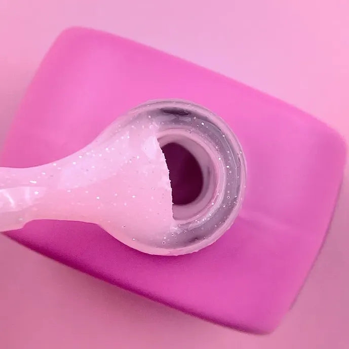 Pink glitter builder gel for nails shown in an open jar with applicator on a pink background