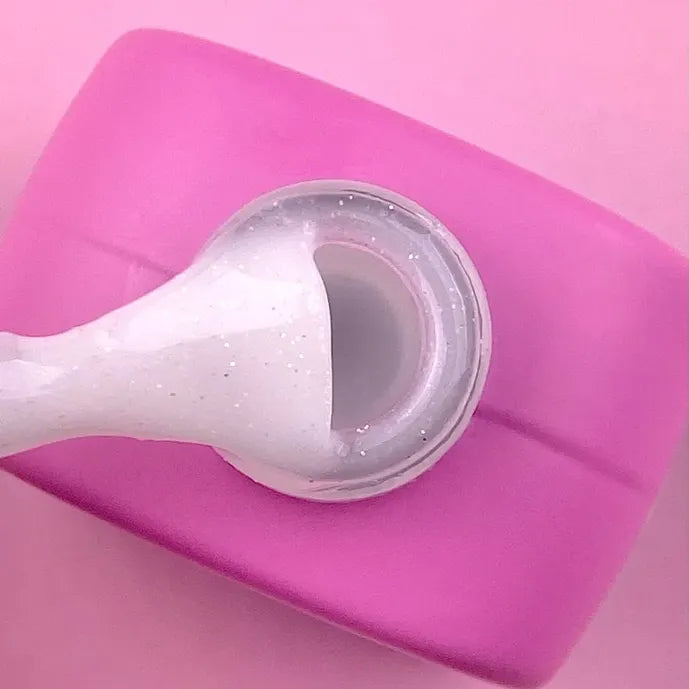 White UV builder gel with glitter texture on a brush above an open pink jar, manicure product