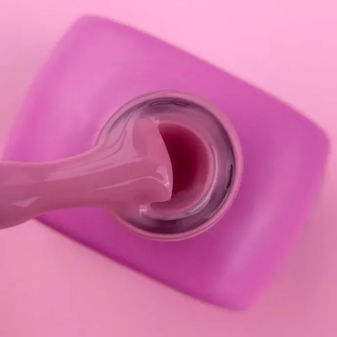 Pink builder gel in an open bottle with applicator, ideal for professional nail extensions