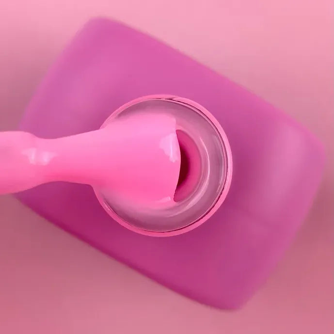 Open bottle of pink UV gel nail polish with applicator, close-up on pink background