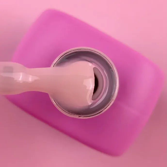 Close-up of pink UV gel nail polish bottle with brush on pink background