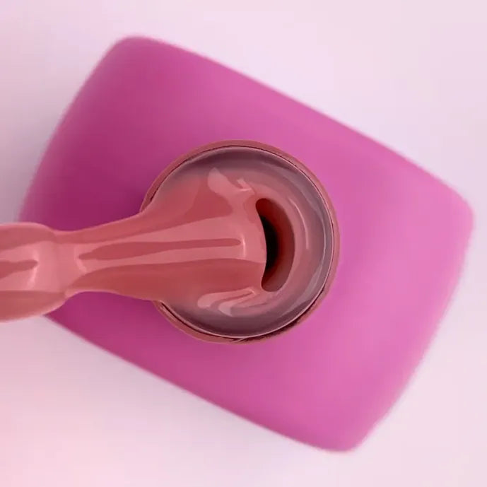 Pink acrylic gel being dispensed from a tube for nail extensions on a pink background