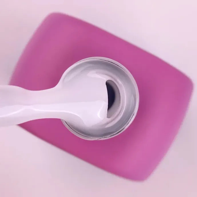 Thick white nail gel being scooped from an open jar with a pink square lid