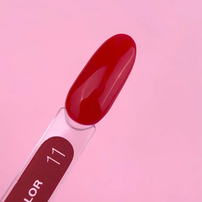 Glossy red gel nail polish color sample on swatch stick against pink background